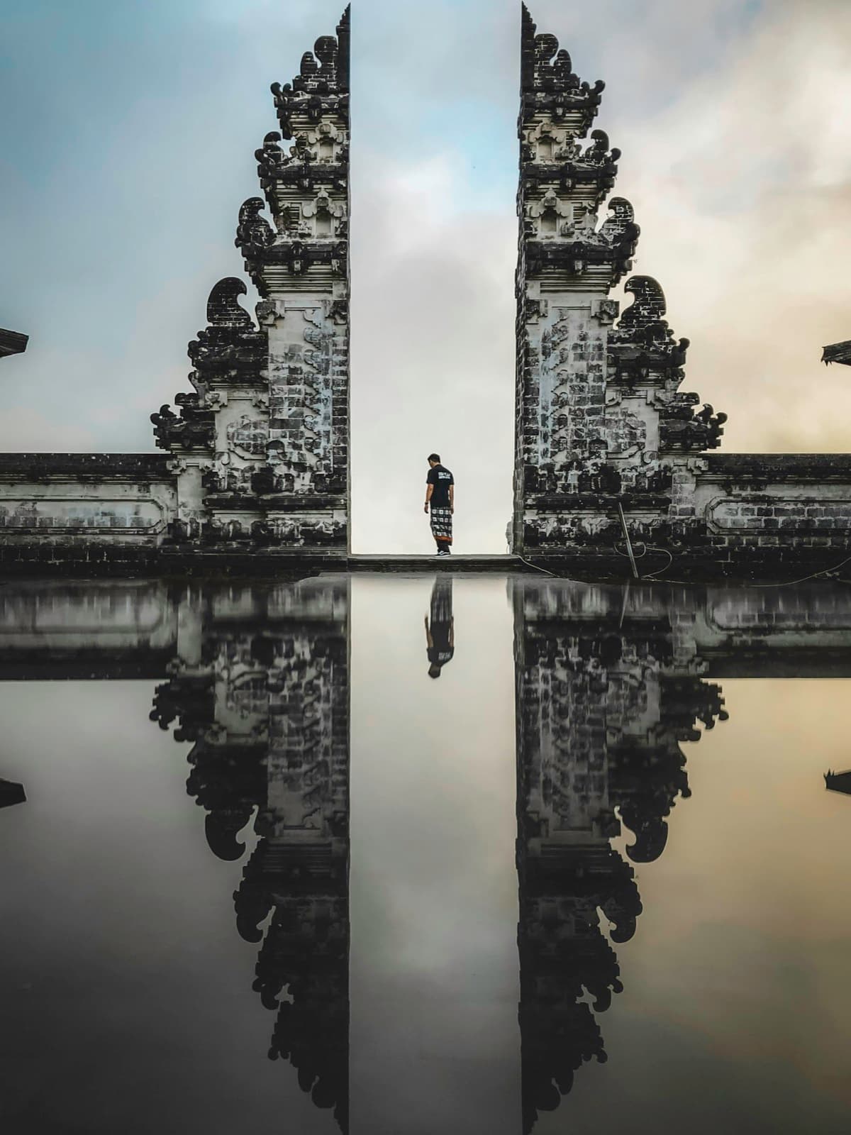 A visitor framed in the split stone gateway at Pura Lempuyang temple, Bali, reflected in still water
