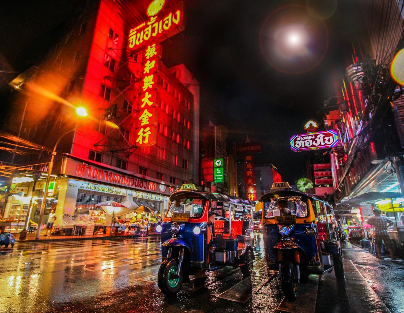 Tuk-tuks parked on a neon-lit street in Bangkok's Chinatown after rain