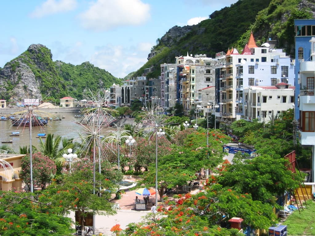 Cat Ba town's waterfront promenade and harbour, with hotels beneath steep green limestone hills