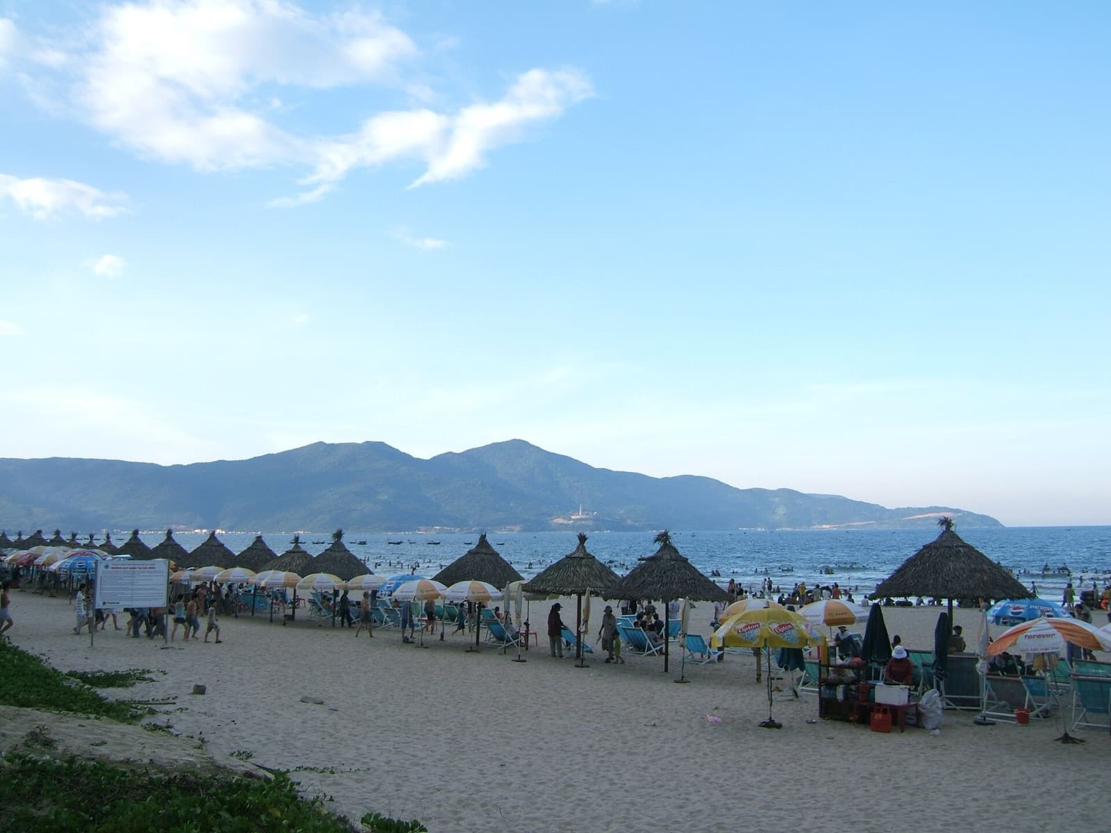 My Khe Beach in Da Nang lined with thatched umbrellas and deckchairs, with green mountains across the bay