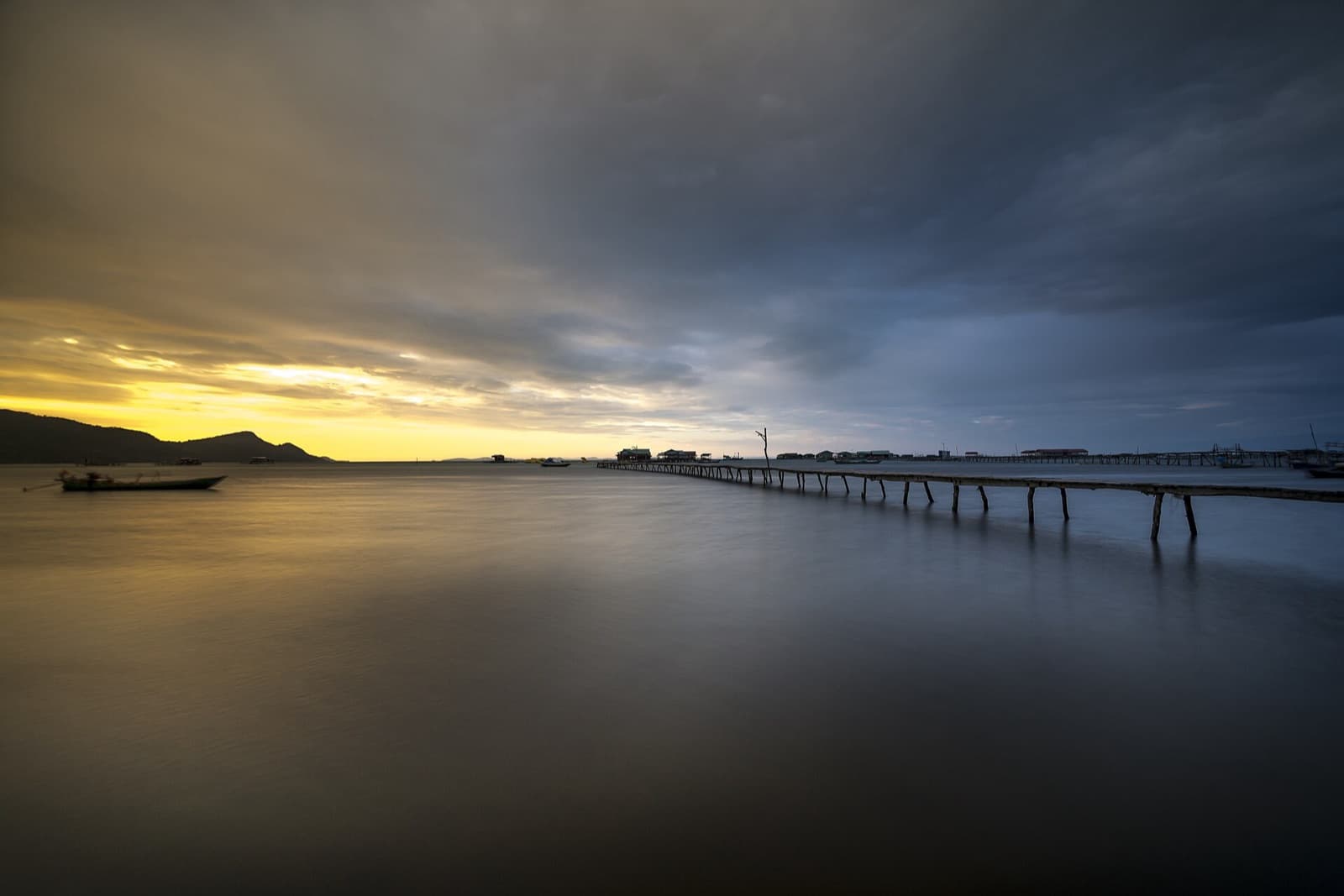 A long wooden jetty and stilt houses reaching into calm water on the Phu Quoc coast at dusk
